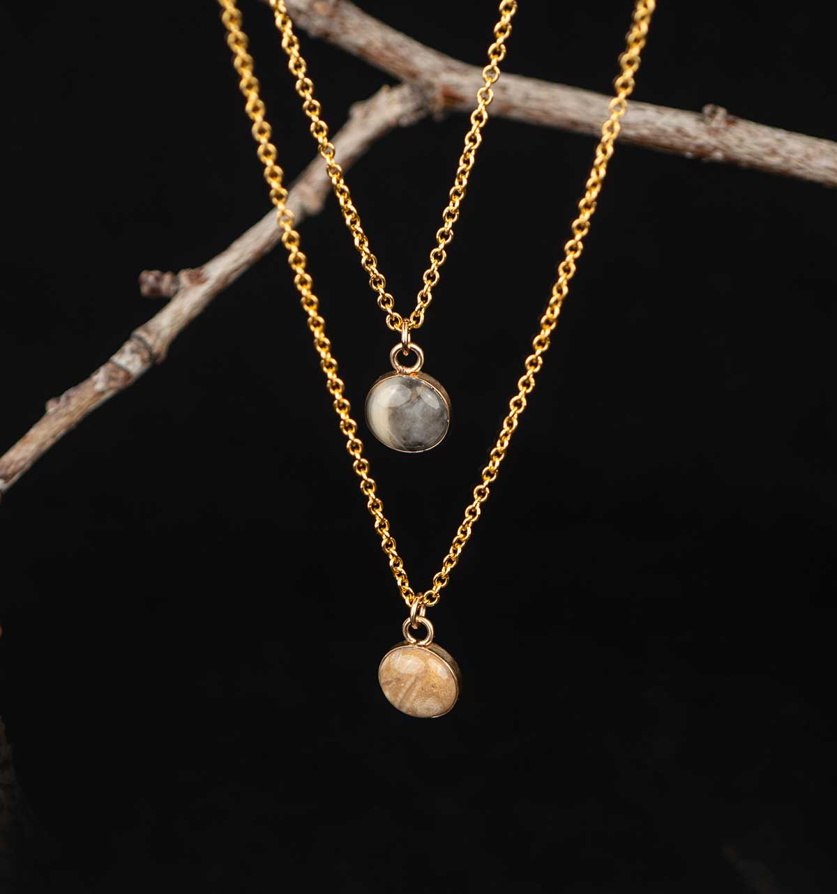 Two gold necklaces with pendant stones on a dark background