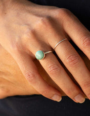 Close-up of a hand wearing a round stone ring with a plain sterling silver band