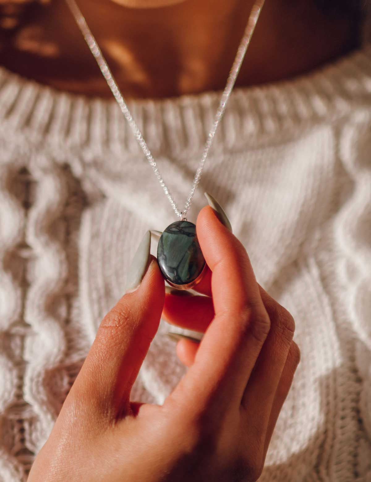 Hand holding a necklace with a green stone pendant