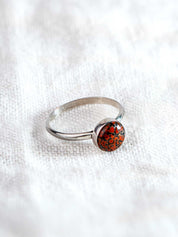 Sterling silver ring with a red and black speckled stone in a round setting