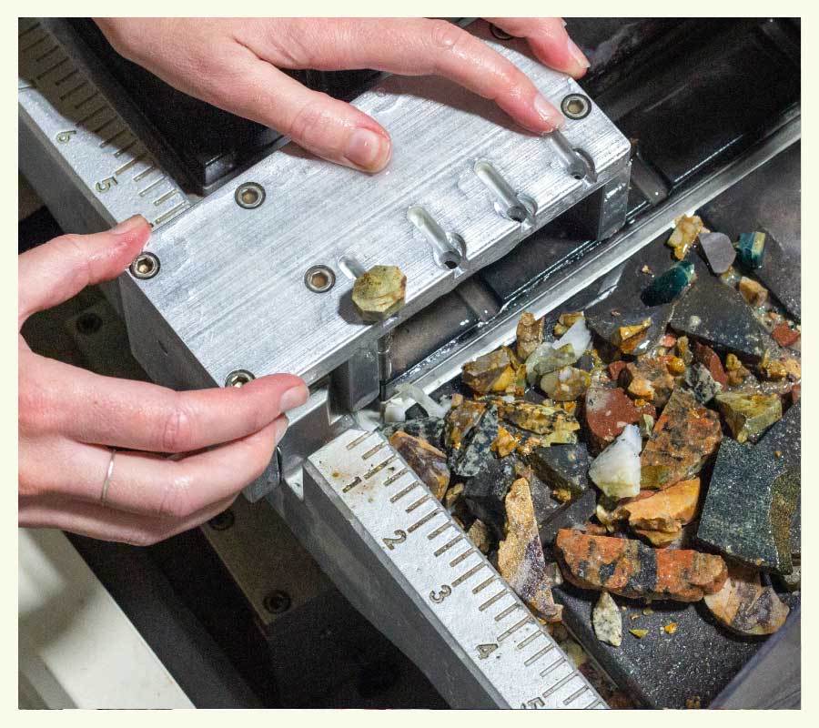Leslie cuts down a rock on a saw with chunks of other rocks scattered beside it