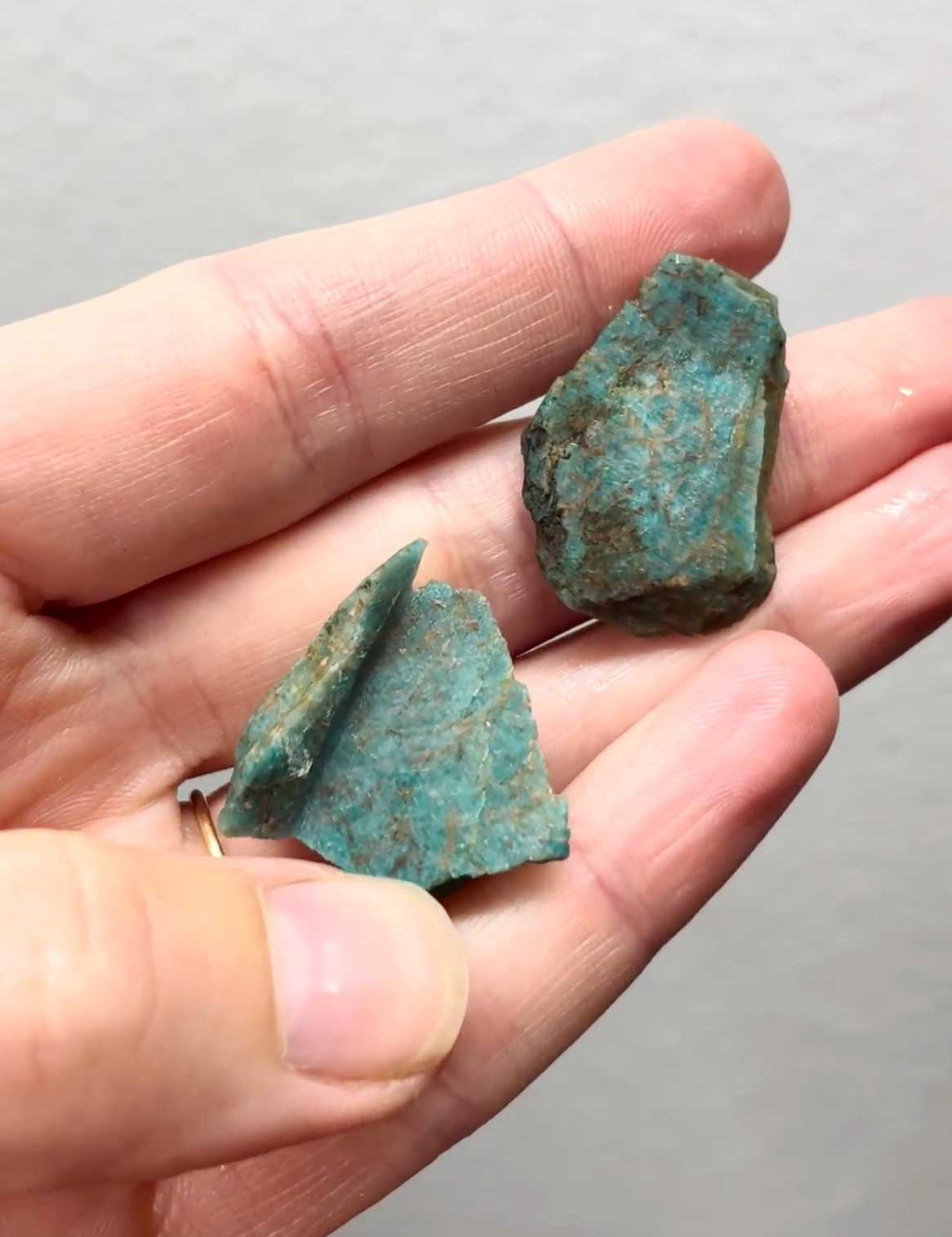 Two chunks of raw blue-green Amazonite held in a hand