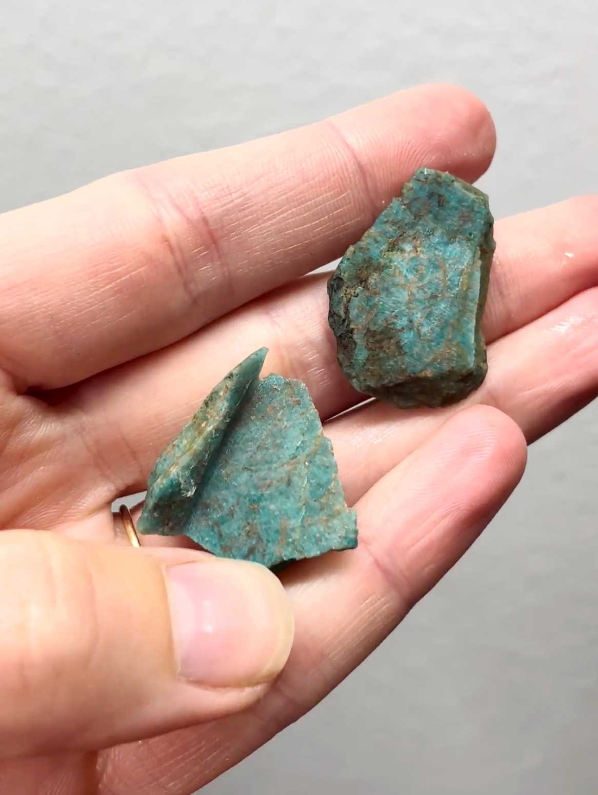 Two chunks of raw blue-green Amazonite held in a hand