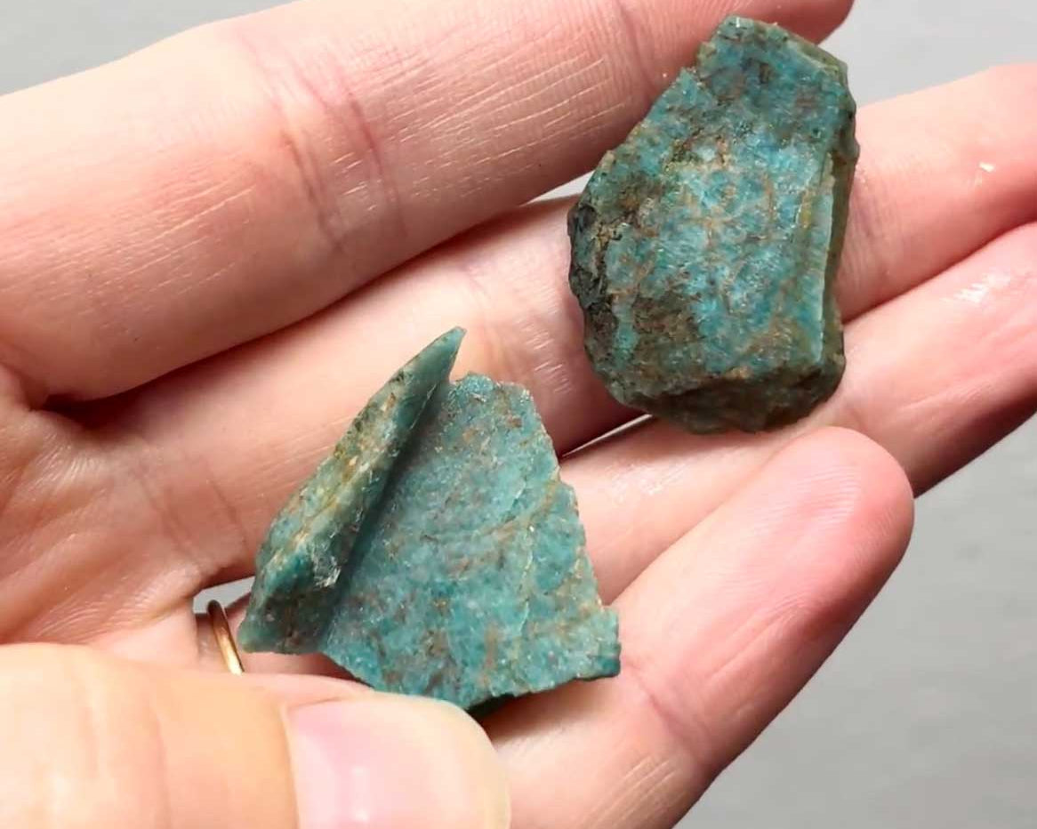 Two chunks of raw blue-green Amazonite held in a hand