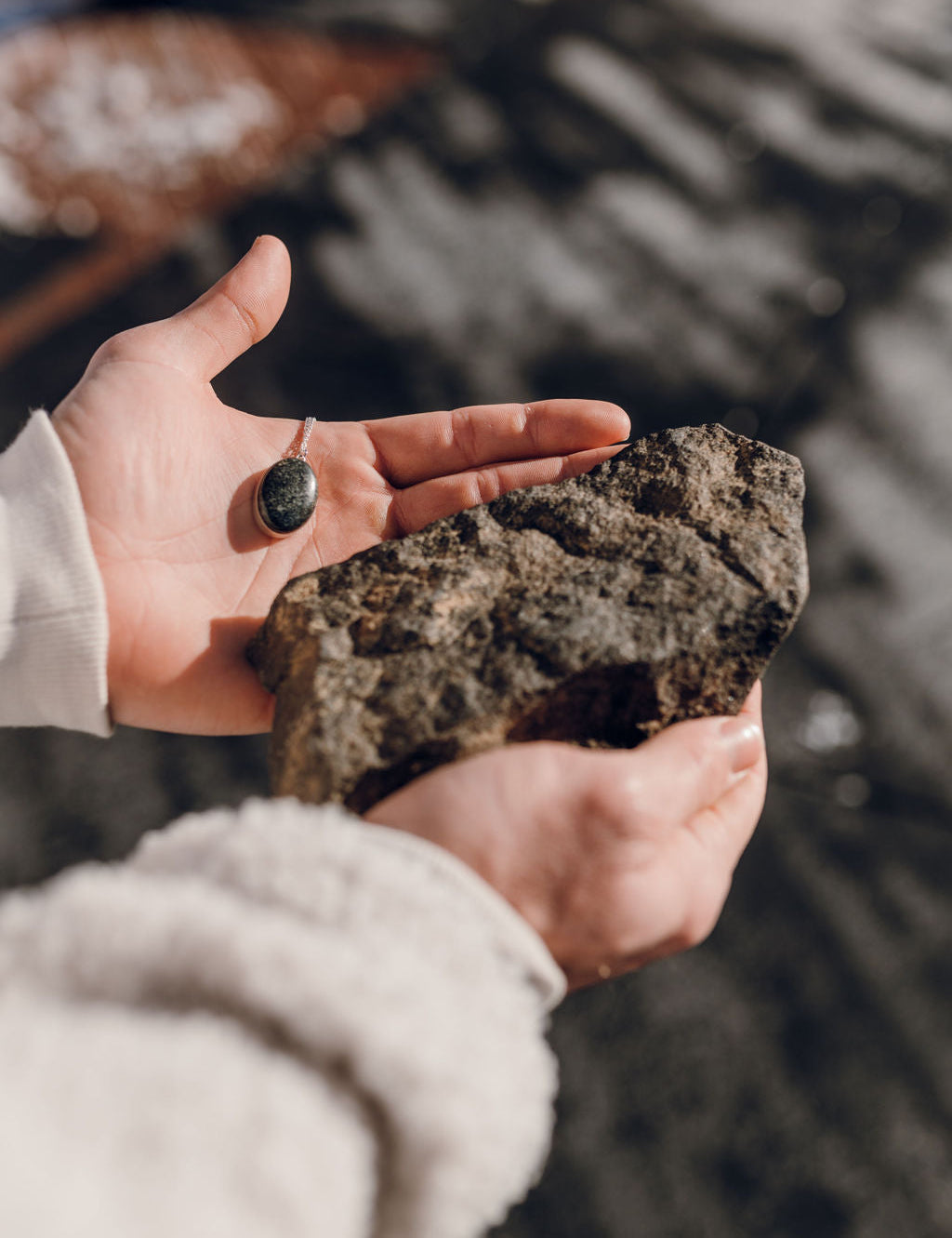 Man in jacket holding a large stone and a stone pendant necklace