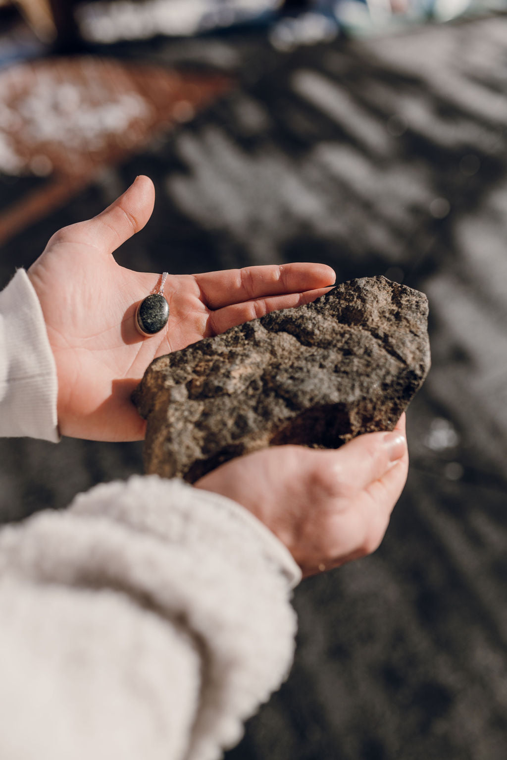 Man in jacket holding a large stone and a stone pendant necklace