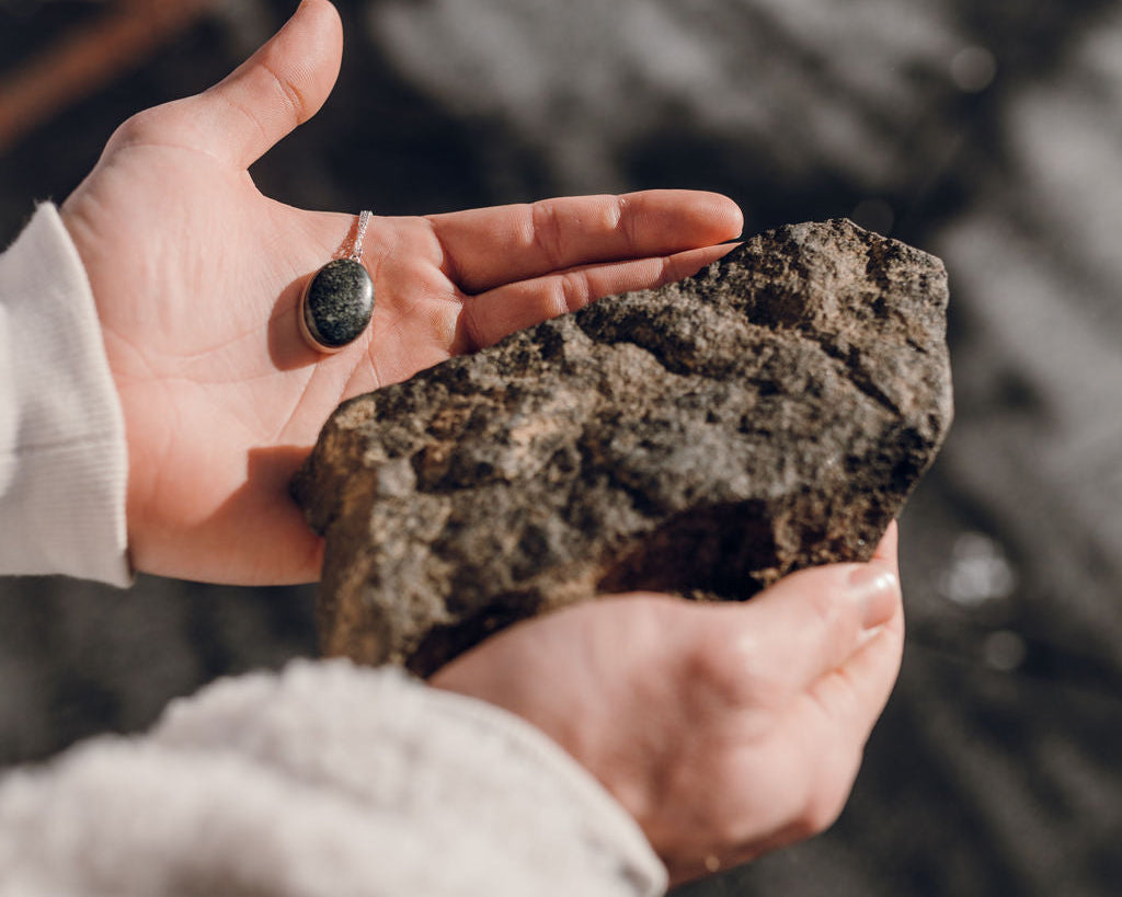 Man in jacket holding a large stone and a stone pendant necklace