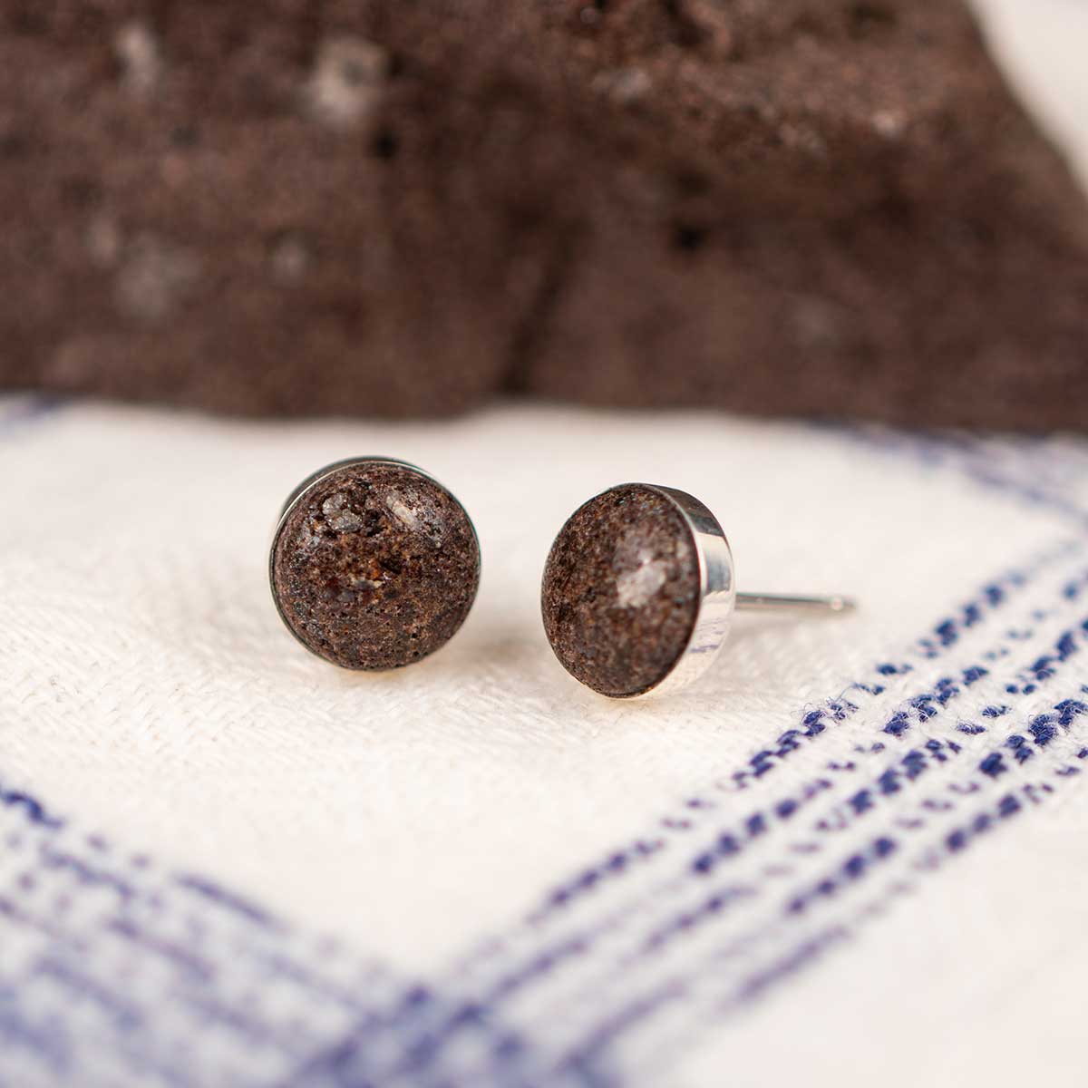 Round stud earrings made from sterling silver set with a natural brown rock on a white and blue striped fabric background.