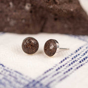 Round stud earrings made from sterling silver set with a natural brown rock on a white and blue striped fabric background.