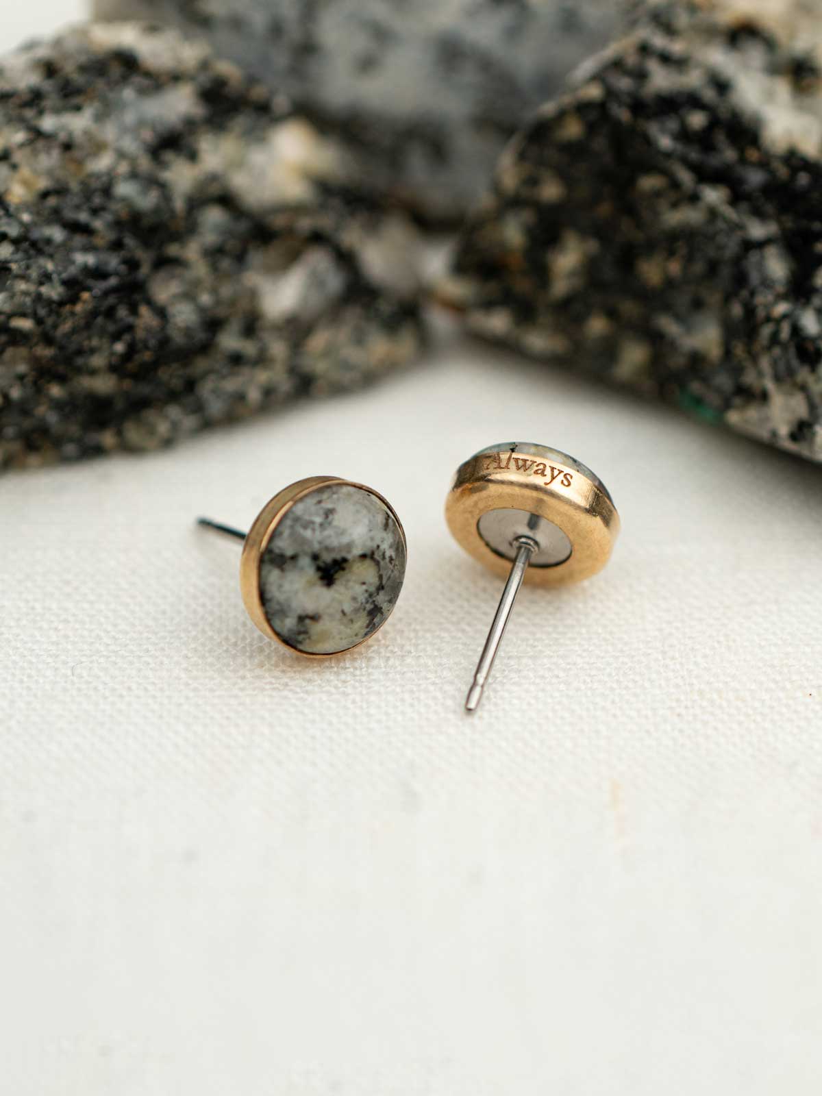 Pair of earrings set in 14k gold fill with natural granite, shown next to the rock they were made from. The edge of the earring is engraved with the word 'always.'