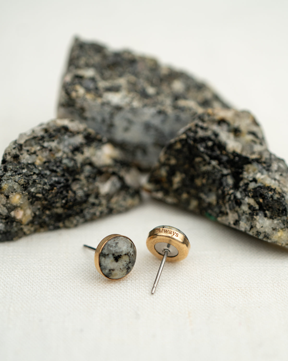 Pair of earrings set in 14k gold fill with natural granite, shown next to the rock they were made from. The edge of the earring is engraved with the word 'always.'