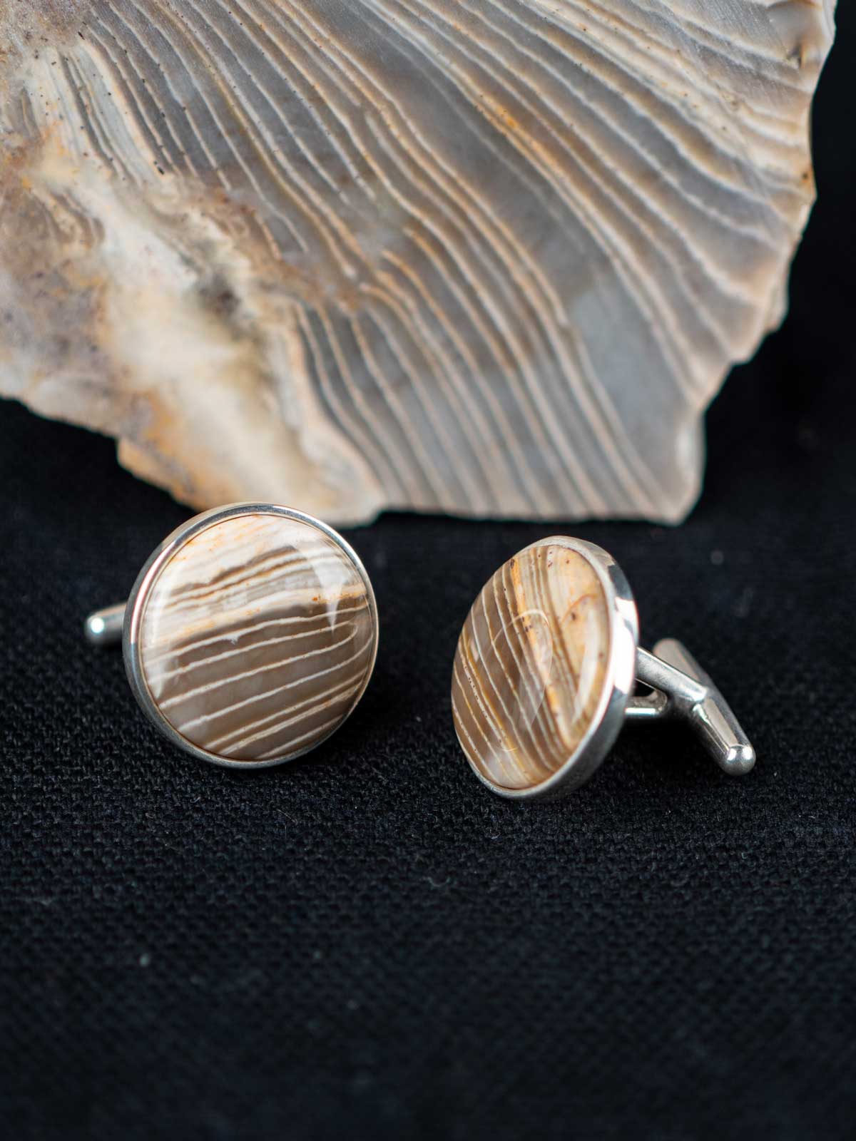 Striped chert cufflinks on a dark textured surface with the stone they were made from in the background