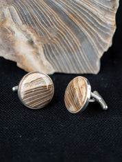 Striped chert cufflinks on a dark textured surface with the stone they were made from in the background
