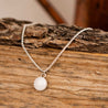 Necklace with a white stone pendant and sterling silver box chain on a wooden log