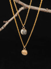 Two gold necklaces with stone pendants on a dark background
