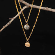 Two gold necklaces with stone pendants on a dark background