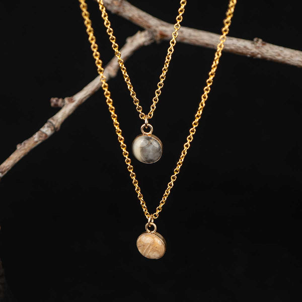 Two gold necklaces with stone pendants on a dark background