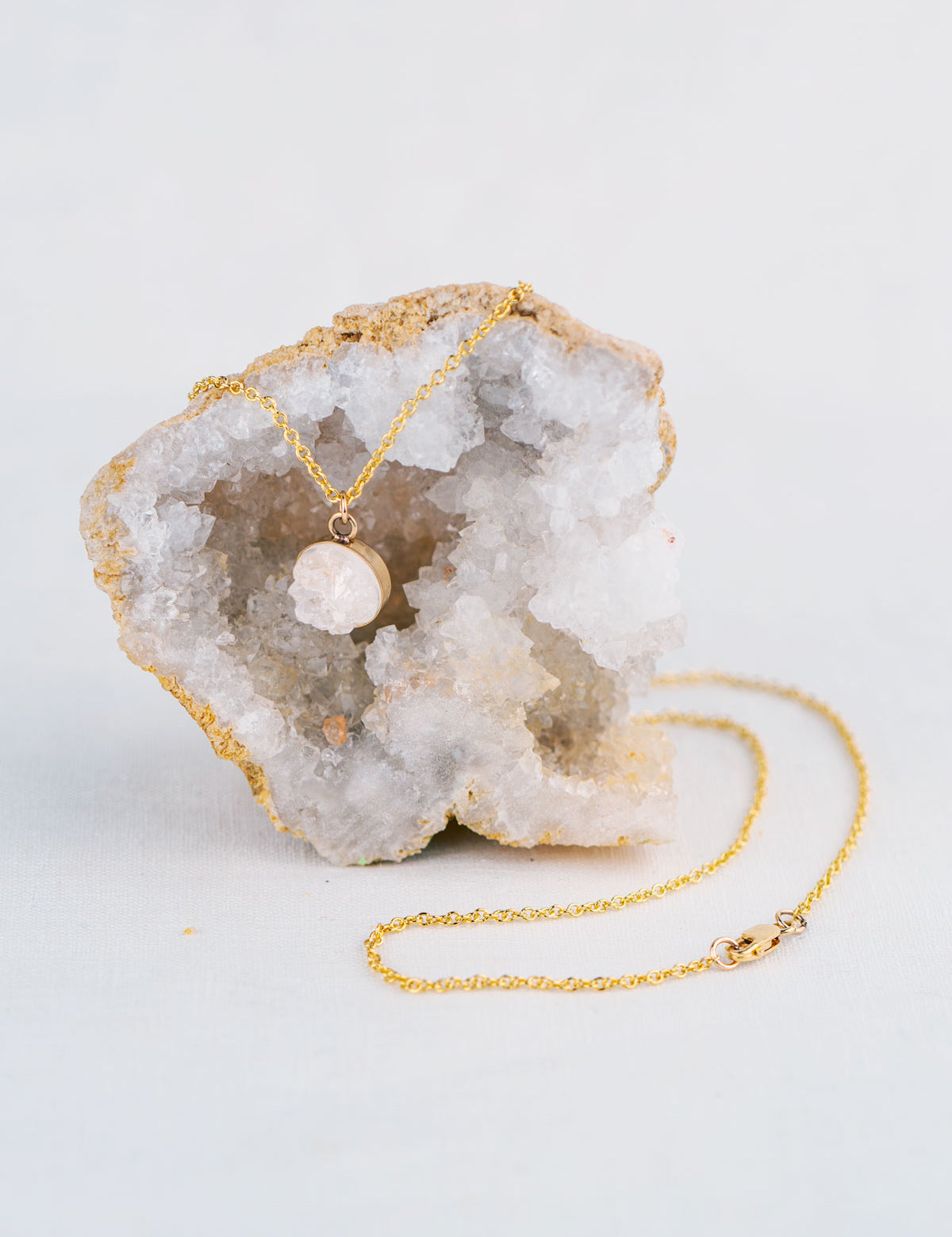 Dainty 14k gold fill pendant necklace made from roughly cut white quartz that came from the geode the necklace is displayed on