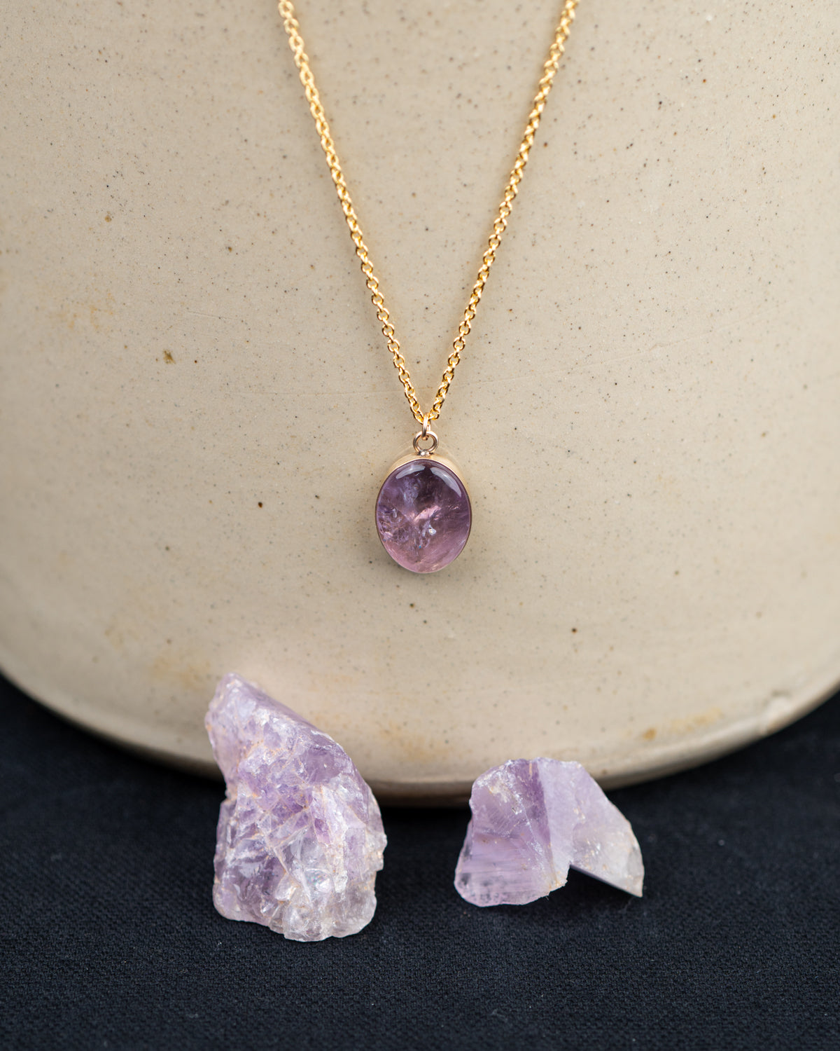 Gold fill necklace with a purple quartz pendant hanging above the amethyst crystals it was made from
