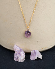 Gold fill necklace with a purple quartz pendant hanging above the amethyst crystals it was made from