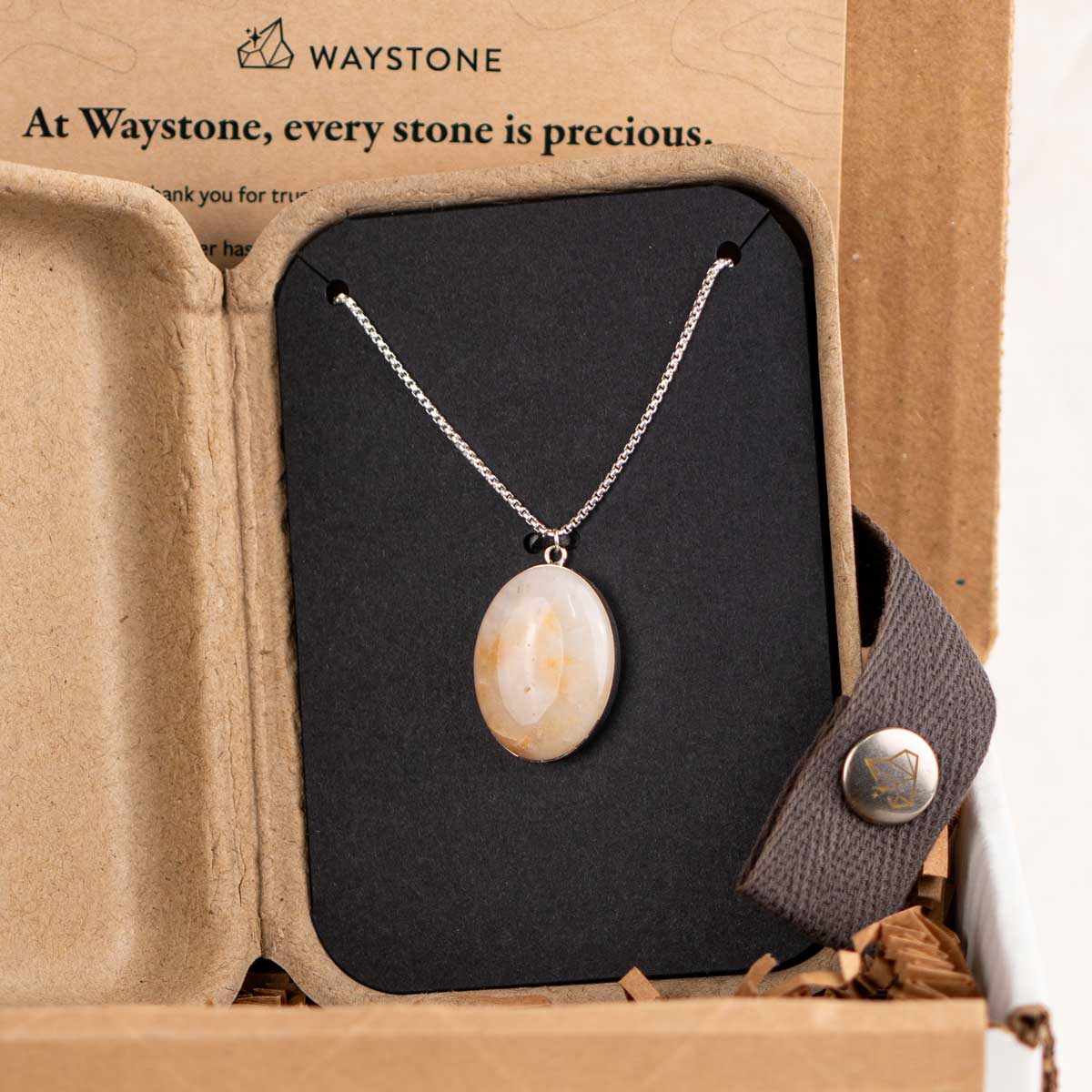 Oval pendant necklace made from a cream colored rock packaged in a kraft gift box