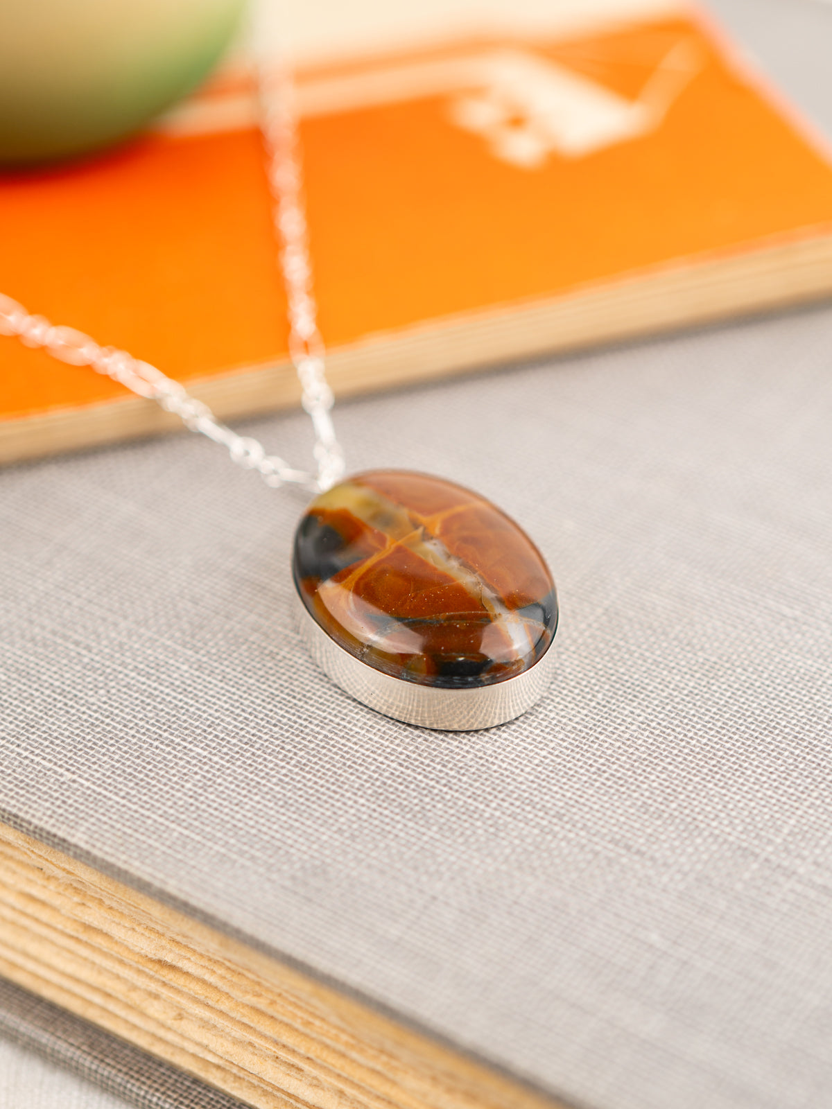 Necklace with an orange and black oval stone pendant in a sterling silver setting