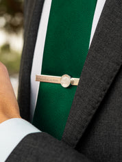 Man in a gray suit wearing a green tie with a sterling silver tie clip that has engraving on the front and a custom quartz stone setting
