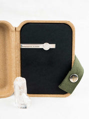 Sterling silver tie clip with engraving set with a round polished quartz stone, displayed in a kraft gift box with the original crystal it was made from