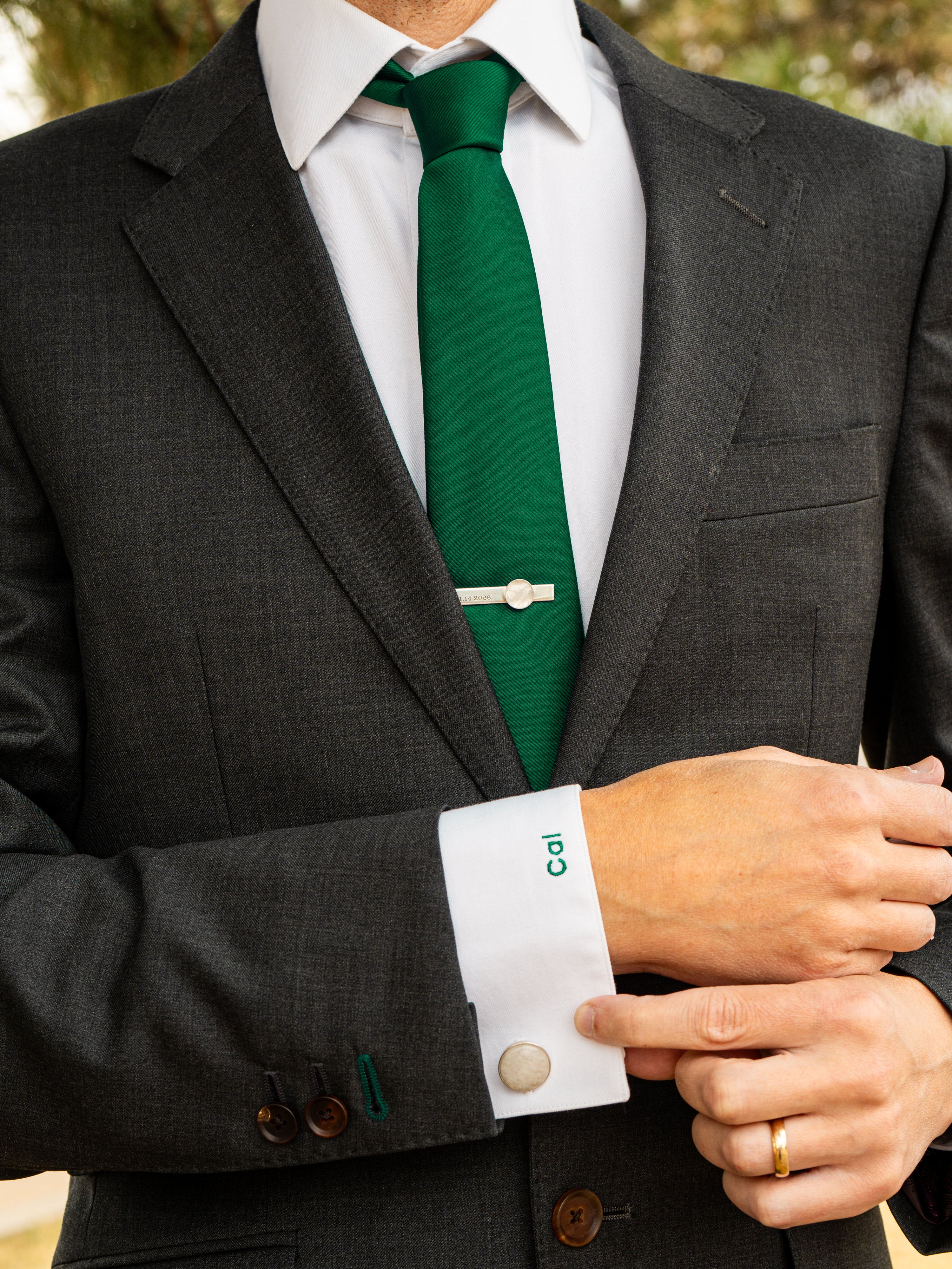 Person wearing a gray suit with a green tie that has a sterling silver tie clip set with a round polished chunk of quartz
