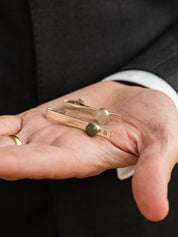 Two engraved sterling silver tie bars set with different sizes of round polished stone, held in a hand