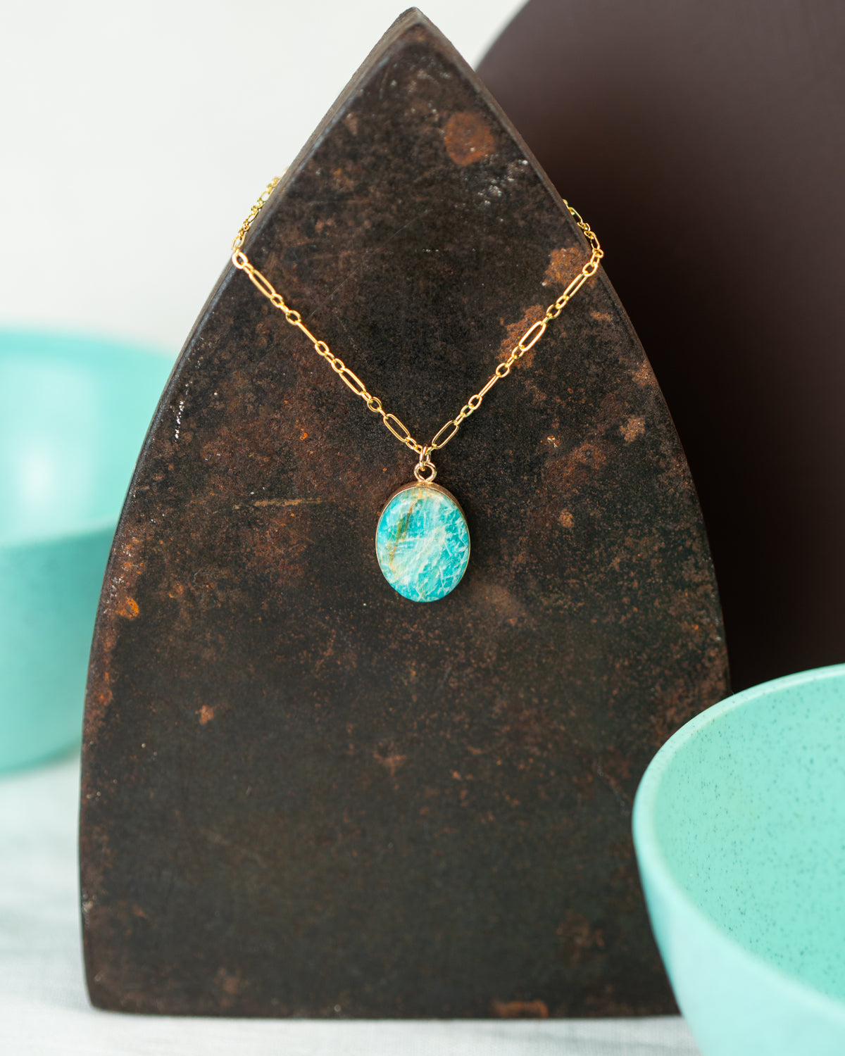 Closeup of an oval pendant made of 14k gold fill hung on a cable chain and set with polished Amazonite