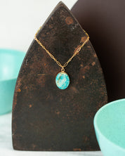 Closeup of an oval pendant made of 14k gold fill hung on a cable chain and set with polished Amazonite