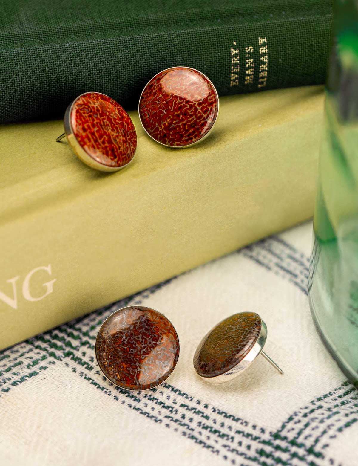 Large round stud earrings made from fossilized dinosaur bone sitting on a stack of books