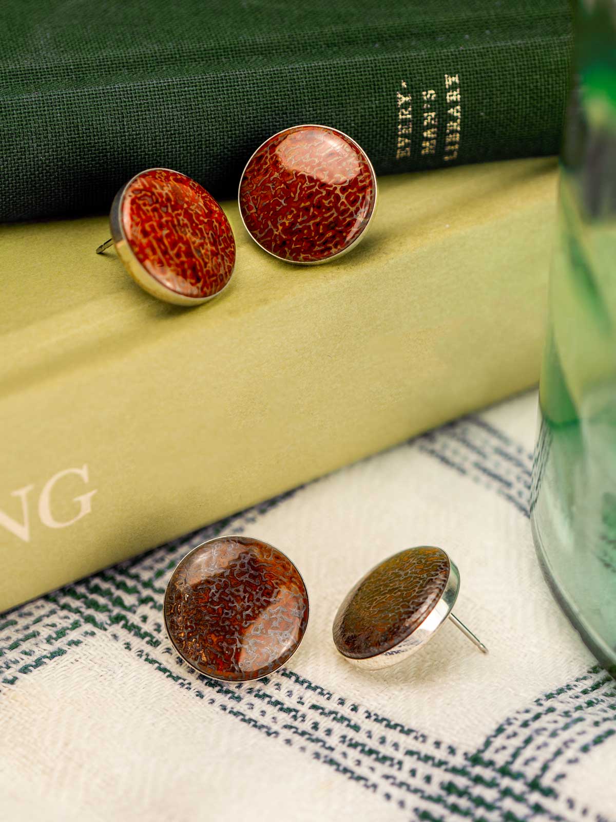 Large round stud earrings made from fossilized dinosaur bone sitting on a stack of books