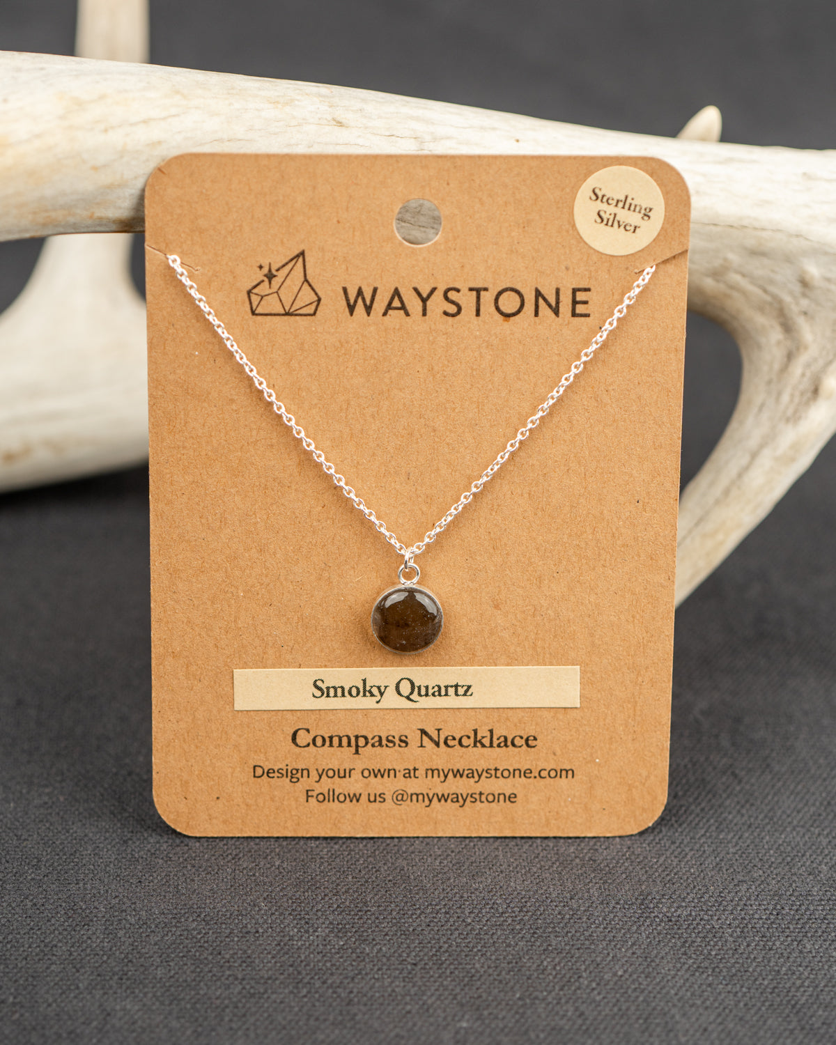 Waystone smoky quartz compass necklace on a brown card with deer antlers in the background