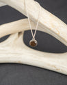 Sterling silver necklace with a round gray stone pendant on a branch against a dark background