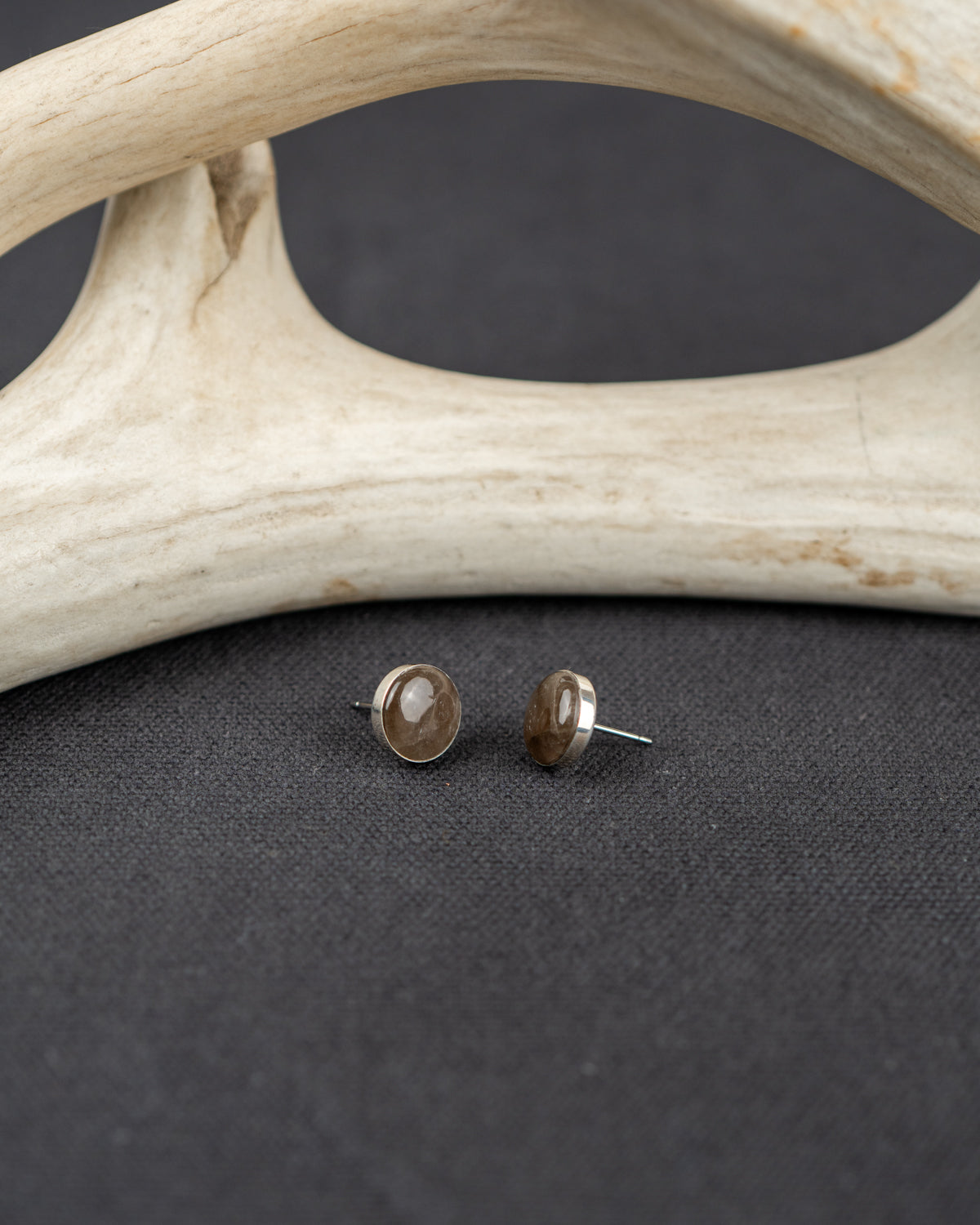 Pair of Smoky Quartz stud earrings on a dark surface with antler decor.