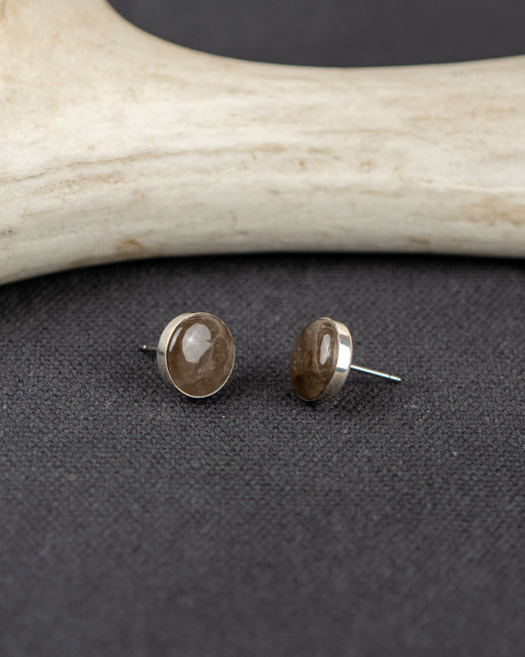 Pair of Smoky Quartz stud earrings on a dark surface with antler decor.
