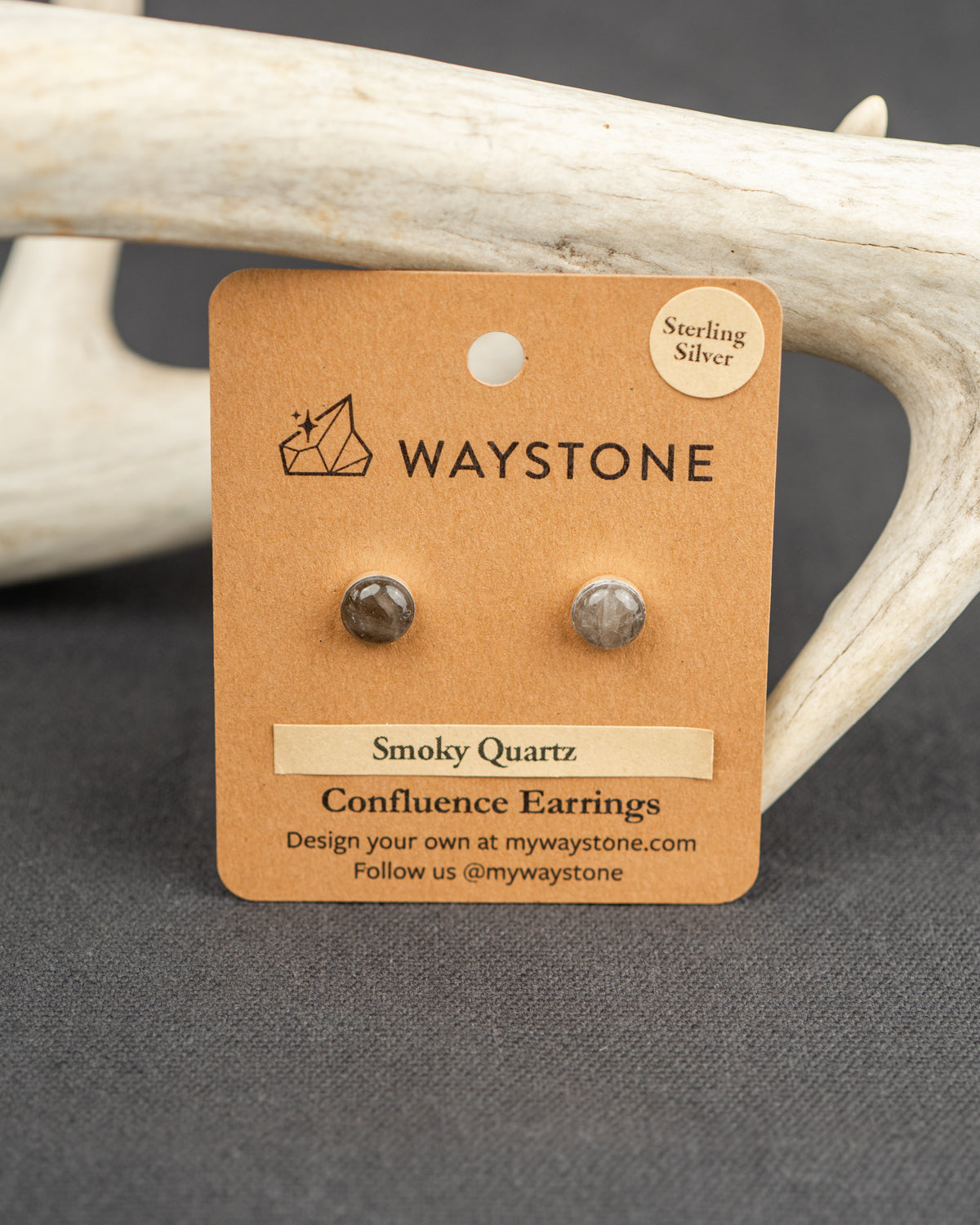 Waystone smoky quartz confluence stud earrings on a kraft paper card with antlers in the background