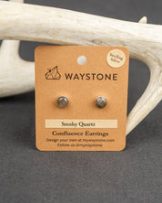Waystone smoky quartz confluence stud earrings on a kraft paper card with antlers in the background