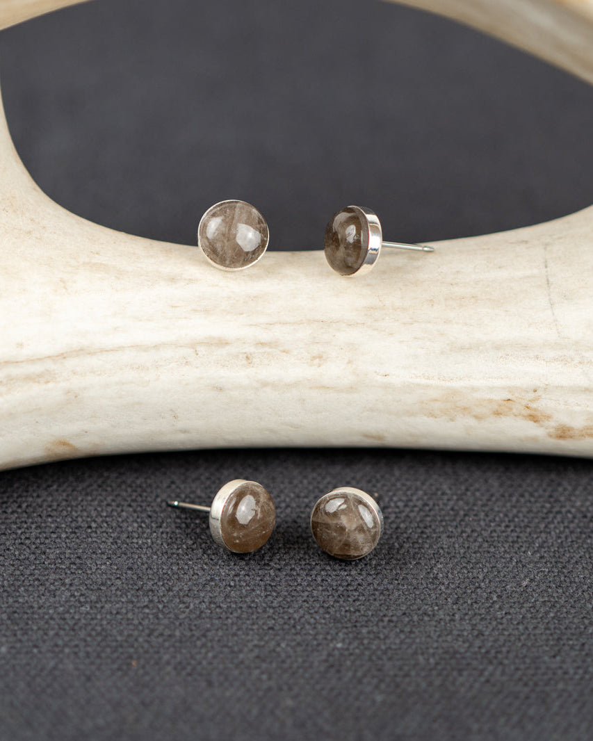Sterling silver stud earrings set with gray smoky quartz stones on a dark surface with antlers in the background