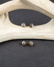 Sterling silver stud earrings set with gray smoky quartz stones on a dark surface with antlers in the background