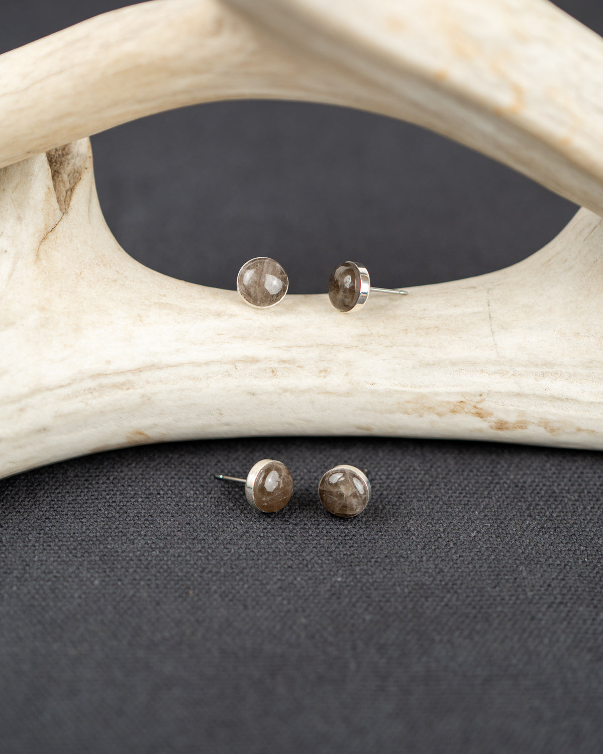 Sterling silver stud earrings set with gray smoky quartz stones on a dark surface with antlers in the background