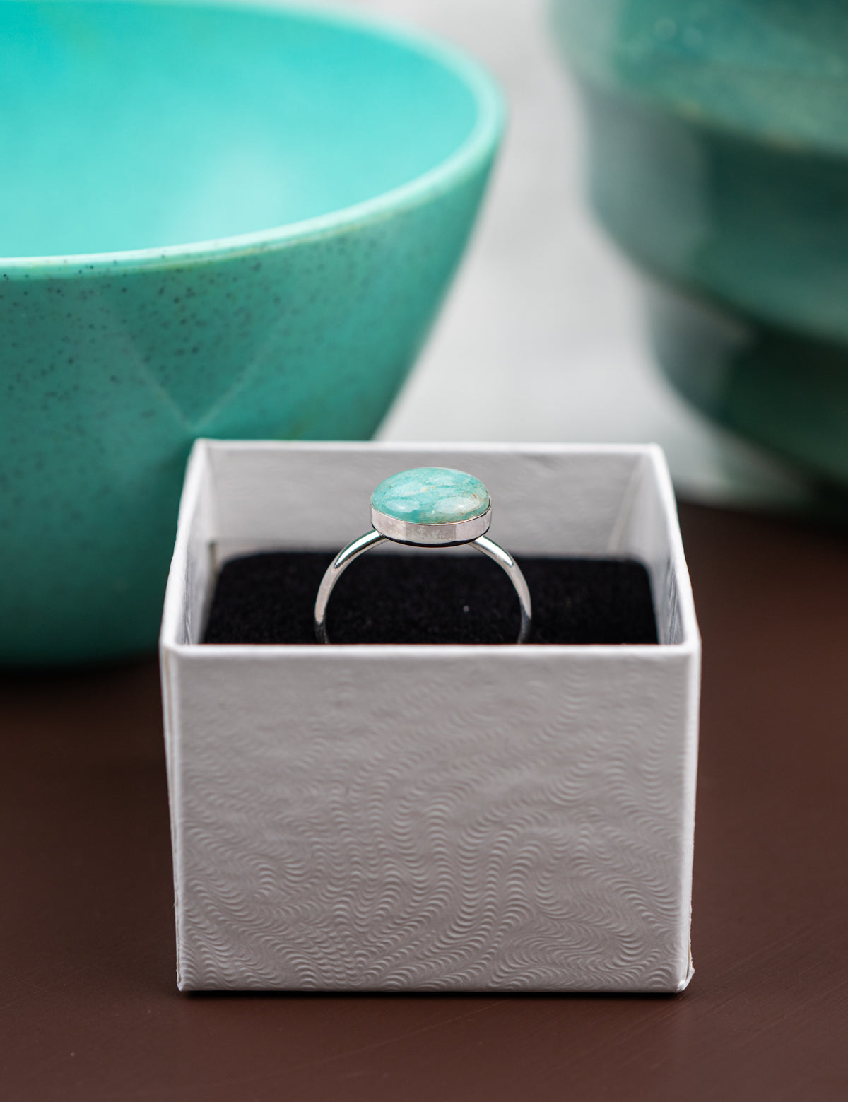 Ring with Amazonite stone in a white box on a brown surface with teal bowls in the background