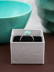 Ring with Amazonite stone in a white box on a brown surface with teal bowls in the background