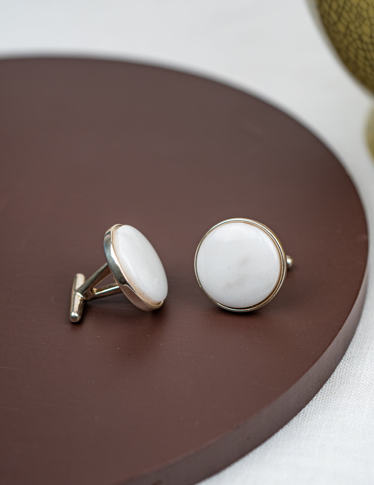 Pair of cufflinks with white stones on a brown circular surface