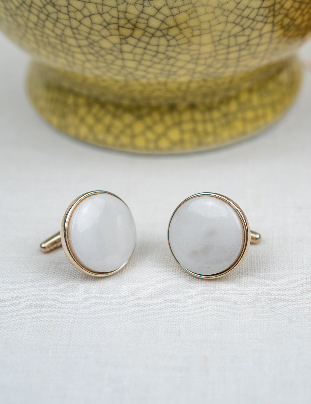 Pair of cufflinks with white stones and gold borders on a light background