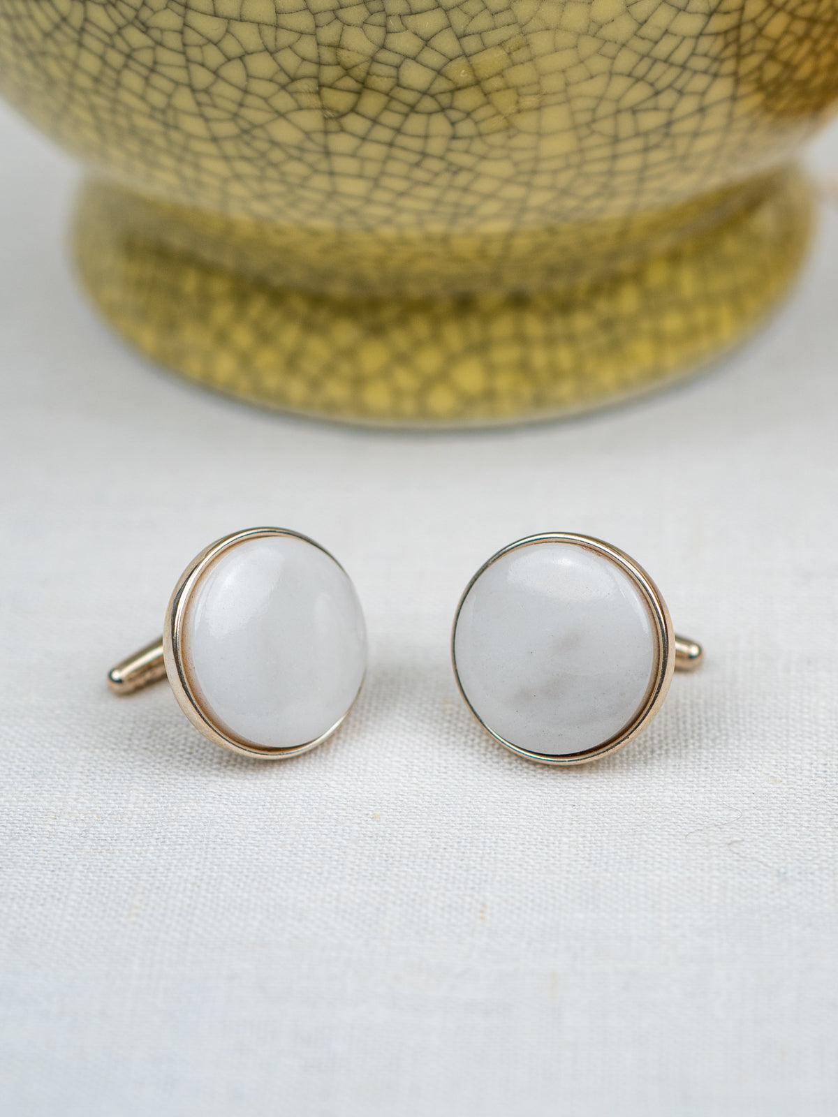 Pair of cufflinks with white stones and gold borders on a light background