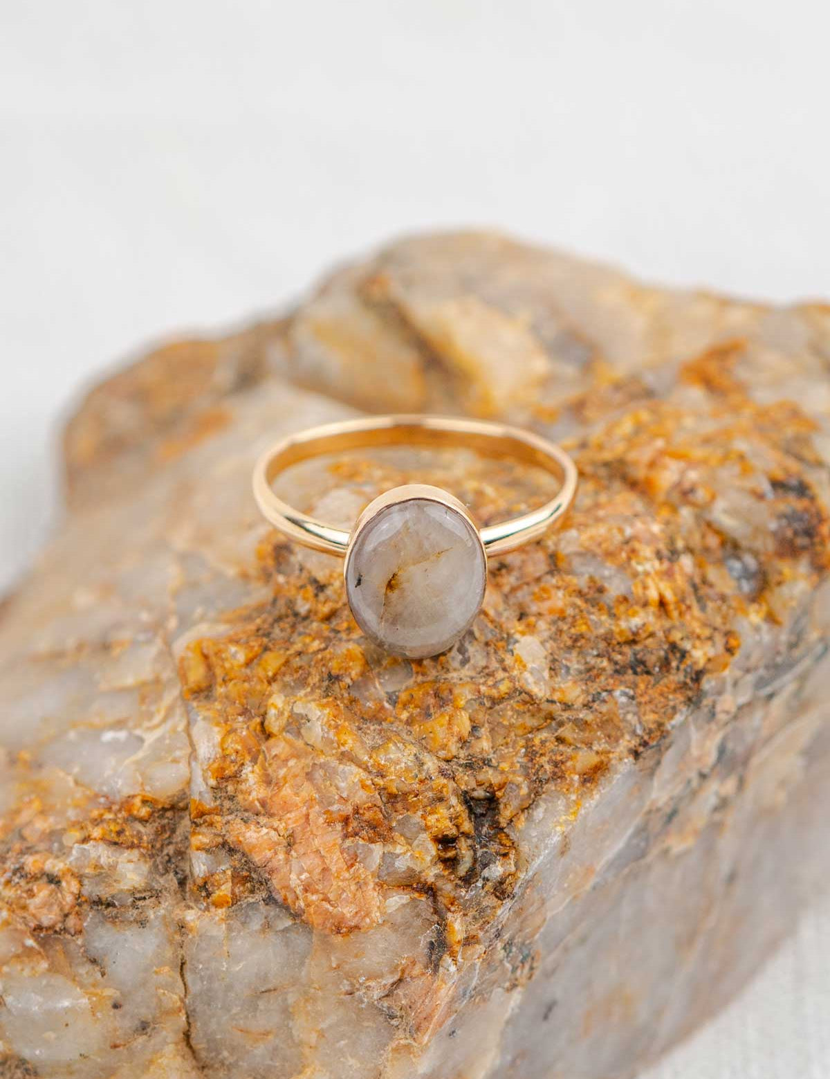 Gold ring with a polished oval stone sitting on the rock it was made from