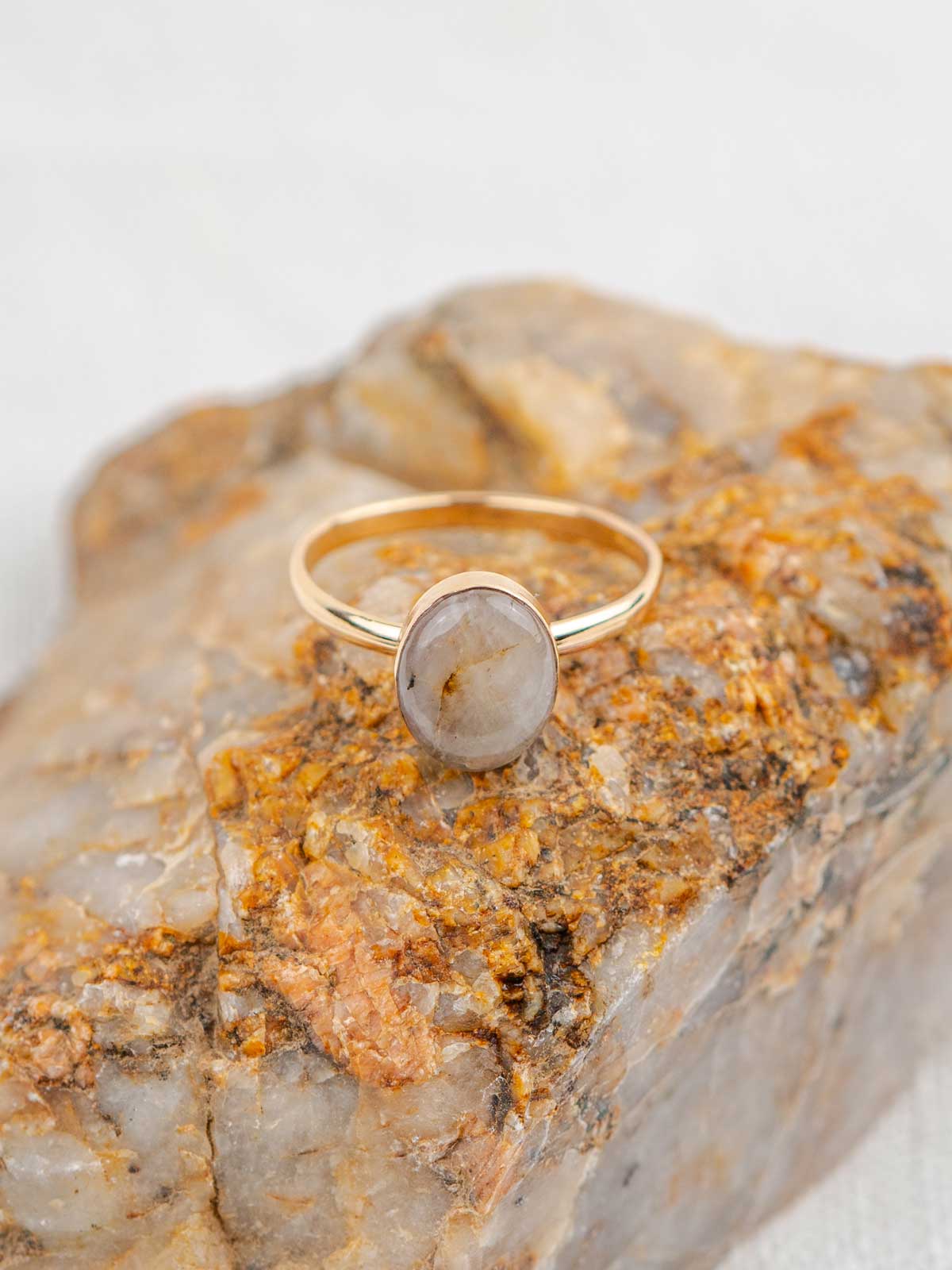 Gold ring with a polished oval stone sitting on the rock it was made from